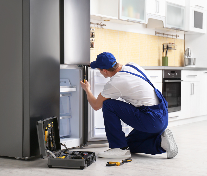 tecnico in ginocchio aggiusta il frigo con utensili in mano